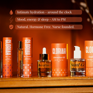 A set of Gloriah Intimate Care products arranged on a wooden shelf against a warm orange-brown background. Visible items include cylindrical orange boxes, a slim amber bottle, a dropper bottle, and a clear bottle with a white pump.