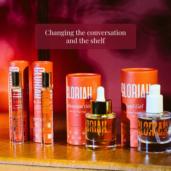 Six GLORIAH skincare products arranged on a wooden surface against a dark red background, including two cylindrical tubes, one small dropper bottle, one clear bottle with amber liquid, and one clear bottle with white dropper cap. A dark red banner at the top reads, 'Changing the conversation and the shelf.