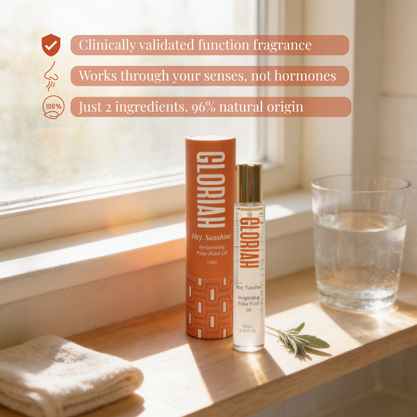 A GLORIAH Hey Sunshine fragrance oil bottle and matching orange cylindrical box sit on a wooden windowsill with warm natural light. A glass of water, a folded towel, and a sprig of rosemary are nearby, with marketing text callouts on the left.