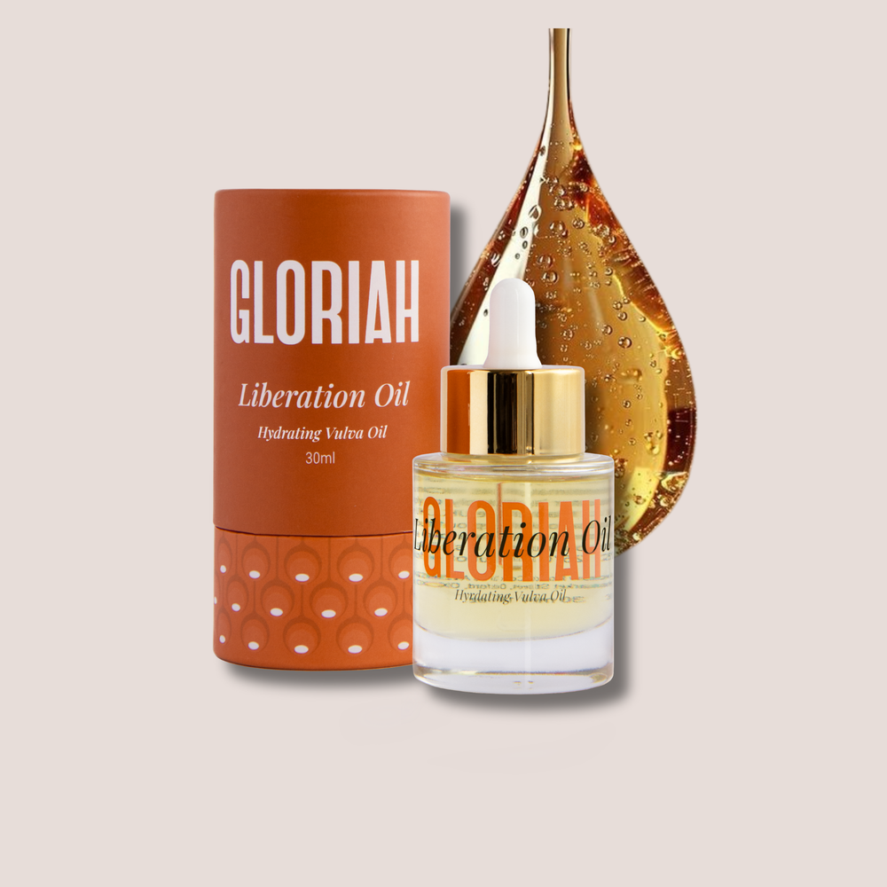 A bottle of GLORIAH Liberation Oil with a gold dropper cap stands in front of its orange cylindrical packaging and a large golden teardrop graphic on a light beige background.