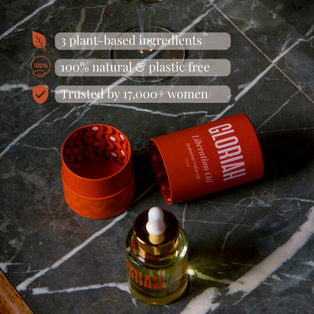 A bottle of GLORIAH Liberation Oil with a gold dropper cap stands in front of its orange cylindrical packaging and a large golden teardrop graphic on a light beige background.
