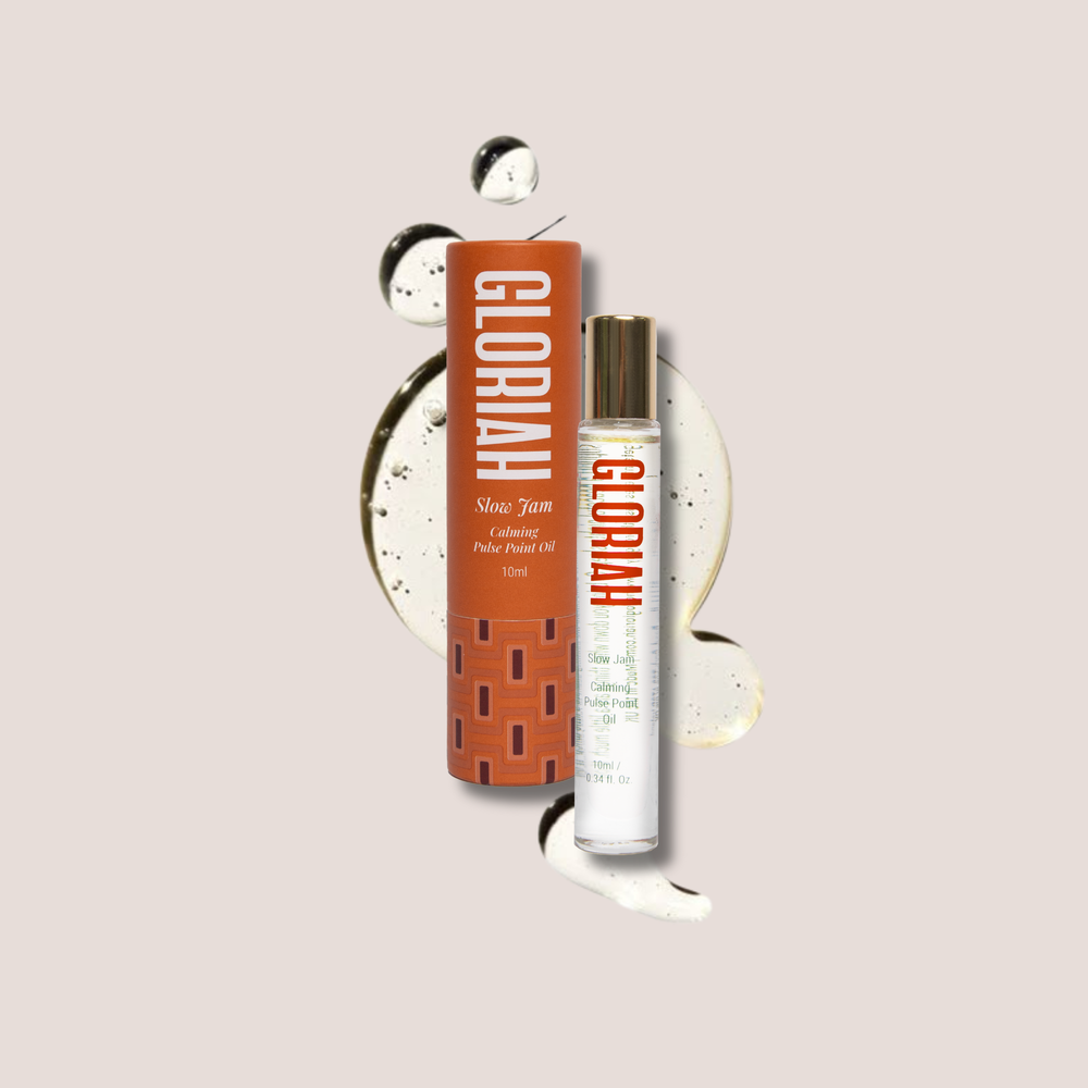 A bottle of GLORIAH Slow Jam Roller-Oil next to its orange cardboard packaging box, styled with decorative cream swirls and black-and-white circular elements on a light beige background