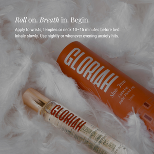 Gloriah Slow Jam roller-oil in a clear bottle with a gold cap, placed on white fluffy faux fur beside an orange bottle, with white text describing how to apply the oil.