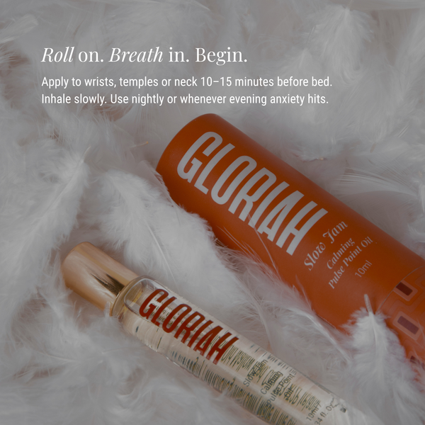 Gloriah Slow Jam roller-oil in a clear bottle with a gold cap, placed on white fluffy faux fur beside an orange bottle, with white text describing how to apply the oil.